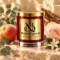 MAISON NOOR Alchemy candle in red glass with gold lid and plaque, styled with eucalyptus, peach, rose and orange blossom.
