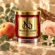 MAISON NOOR Alchemy candle in red glass with gold lid and plaque, styled with eucalyptus, peach, rose and orange blossom.