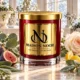 MAISON NOOR Arctic Ivy red glass candle with gold lid, styled with eucalyptus, sage, fig, lemon peel and a pale rose in a bright winter conservatory.