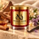 MAISON NOOR Autumn Ambrette red glass candle with gold lid, styled with maple syrup, cinnamon, sandalwood, orange blossom, heliotrope and vanilla on pale stone.