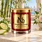MAISON NOOR Azura red glass candle with gold lid, styled with bamboo, bergamot, apple and delicate flowers on an ivory stone pavilion table.