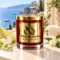 MAISON NOOR Azure Coast red glass candle with gold lid, styled with honeydew melon, apple, lily of the valley and jasmine above an azure coastline.