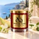 MAISON NOOR Azure Coast red glass candle with gold lid, styled with honeydew melon, apple, lily of the valley and jasmine above an azure coastline.