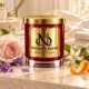 MAISON NOOR Baby Powder red glass candle with gold lid, styled with pale rose, violets, orange blossom and orange peel in a soft ivory dressing room.