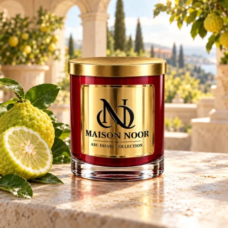 MAISON NOOR Bergamot Element red glass candle with gold lid, styled with bergamot citrus fruits and leaves on ivory stone in a sunlit citrus estate.