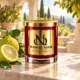 MAISON NOOR Bergamot Element red glass candle with gold lid, styled with bergamot citrus fruits and leaves on ivory stone in a sunlit citrus estate.