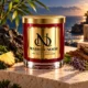 MAISON NOOR Black Coral and Moss red glass candle with gold lid, styled with dark coastal stone, bamboo, lavender, pineapple and wood beside the sea.