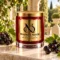 MAISON NOOR Black Currant Element red glass candle with gold lid, styled with fresh black currant clusters and leaves on ivory stone in an elegant garden.