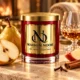 MAISON NOOR Brandied Pear red glass candle with gold lid, styled with pear, apple, cinnamon, cloves and a crystal brandy glass in a warm luxury lounge.