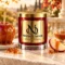 MAISON NOOR Caramel Apple red glass candle with gold lid, styled with a caramel apple, fresh apple slices, caramel and caramelized sugar on ivory stone.