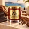 MAISON NOOR Caribbean Teakwood red glass candle with gold lid, styled with teakwood, leather, tobacco leaf, cloves and peppercorns on a Caribbean terrace.