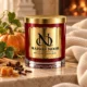 MAISON NOOR Cashmere Pumpkin red glass candle with gold lid, styled with pumpkin, vine leaves, cinnamon, cloves and caramel against cream cashmere.