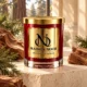MAISON NOOR Cedar Element red glass candle with gold lid, styled with cedar wood and foliage on ivory limestone in an elegant forest retreat.