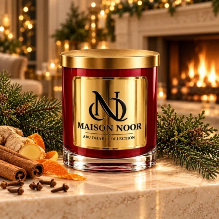 MAISON NOOR Christmas Hearth red glass candle with gold lid, styled with evergreen sprigs, cinnamon, ginger, orange peel and cloves beside a festive fireplace.