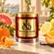 MAISON NOOR Citron and Mandarin red glass candle with gold lid, styled with mandarin, grapefruit, lemon, orange, peach and vanilla on a sunlit terrace.