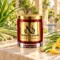 MAISON NOOR Citronella red glass candle with gold lid, styled with citronella grass, lemongrass and lemon peel on ivory stone in a tropical garden spa.