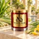 MAISON NOOR Citronella red glass candle with gold lid, styled with citronella grass, lemongrass and lemon peel on ivory stone in a tropical garden spa.