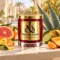 MAISON NOOR Citrus Agave red glass candle with gold lid, styled with agave leaves, grapefruit, mandarin, lime, orange peel and peach on a sunlit terrace.