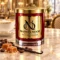 Red MAISON NOOR candle with gold lid on marble beside coffee beans, caramel and vanilla, with a latte behind.