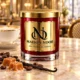 Red MAISON NOOR candle with gold lid on marble beside coffee beans, caramel and vanilla, with a latte behind.