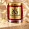 Red MAISON NOOR candle with gold lid on ivory stone beside condensed milk and sugar crystals against ivory silk.