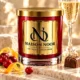 Red MAISON NOOR candle with gold lid beside cranberries, citrus peel and a praline, with a sparkling wine glass behind.
