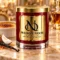 Red MAISON NOOR candle with gold lid on marble beside creme brulee, coconut and vanilla, with an amber glass behind.