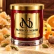 Red MAISON NOOR candle with gold lid surrounded by crystallized ginger, cardamom, citrus peel and nutmeg on ivory stone.