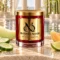 Red MAISON NOOR candle with gold lid beside cucumber, honeydew, cantaloupe and lime, with water and bamboo behind.