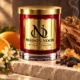 Red MAISON NOOR candle with gold lid beside orange blossom, orange, cedar wood, cloves, tonka beans and incense resin.