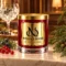 Red MAISON NOOR candle with gold lid beside juniper berries, red currants and cypress, with a gin glass in a wood-paneled setting.
