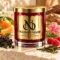 Red MAISON NOOR candle with gold lid beside elderberries, mandarin, raspberries, green tea and pink geranium on ivory stone.