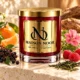 Red MAISON NOOR candle with gold lid beside elderberries, mandarin, raspberries, green tea and pink geranium on ivory stone.