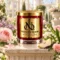 Red MAISON NOOR candle with gold lid surrounded by rose, jasmine, lilac, lily of the valley, carnation and pear in a bright conservatory.