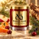 Red MAISON NOOR candle with gold lid beside apple, mandarin, cranberries, fir and juniper on ivory stone.