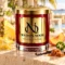 Red MAISON NOOR candle with gold lid beside pineapple, starfruit, peach, jalapeno, vanilla and caramel in a tropical terrace setting.