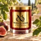 Red MAISON NOOR candle with gold lid on ivory stone beside fresh figs and green fig leaves in warm daylight.