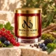 Red MAISON NOOR candle with gold lid beside red currants, blackberries, blueberries, peppercorns and moss on ivory stone.