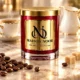 Red MAISON NOOR candle with gold lid beside roasted coffee beans and sugar cubes, with a coffee cup and cream pitcher behind.