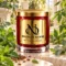 Red MAISON NOOR candle with gold lid framed by mint, eucalyptus and tomato leaves, with anise seeds on ivory stone.