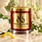 Red MAISON NOOR candle with gold lid beside white gardenia, tuberose, jasmine and lemon peel on ivory stone.