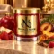 Red MAISON NOOR candle with gold lid beside apple, strawberry, plum, peach and raspberries in a warm elegant salon.
