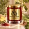 Red MAISON NOOR candle with gold lid beside ginger, saffron, cardamom, nutmeg, citronella grass and evergreen foliage.