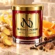 Red MAISON NOOR candle with gold lid beside ginger, citrus, sugar, vanilla, cinnamon, cloves, nutmeg and allspice.