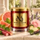 Red MAISON NOOR candle with gold lid beside grapefruit, mint, rhubarb, pink rose, lavender, apple and vanilla on ivory stone.