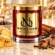Red MAISON NOOR candle with gold lid beside ginger, citrus peel, molasses, cinnamon, vanilla, chestnuts, cloves and nutmeg on ivory marble.