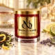 Red MAISON NOOR candle with gold lid beside black tea leaves, lemon, bergamot and lavender, with a porcelain tea cup behind.