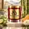 Red MAISON NOOR candle with gold lid beside aloe, lime, cantaloupe, chrysanthemum and moss, with bamboo and misty mountains behind.