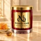 Red MAISON NOOR candle with gold lid on ivory stone beside honeycomb, honey and a gold honey dipper.