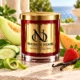 Red MAISON NOOR candle with gold lid beside honeydew melon, cantaloupe, cucumber, strawberry, bergamot peel and vanilla on ivory stone.